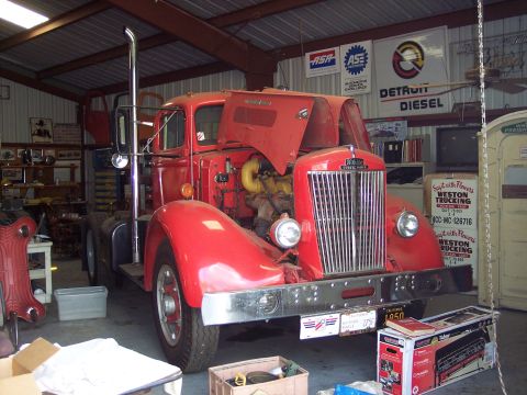 1981 Kenworth W900A - A red semi-truck is parked inside a garage with its hood open, revealing the engine. The license plate indicates the year 1950.