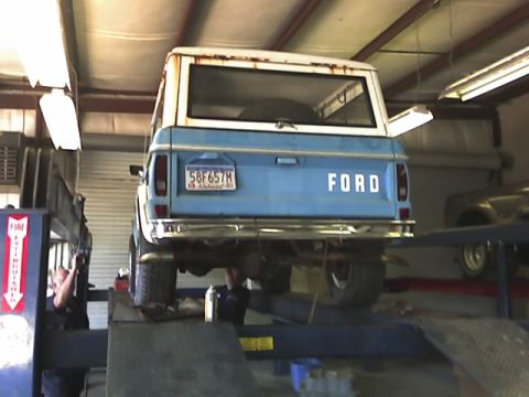 1996 Ford Bronco - A blue Ford Bronco with a white top is raised on a vehicle lift in a garage.