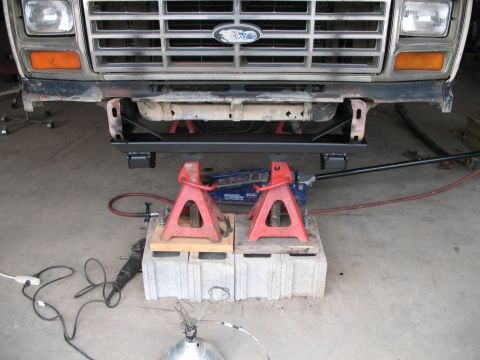 1985 Ford Bronco - Front view of a Ford truck's undercarriage, supported by jack stands and a hydraulic jack.