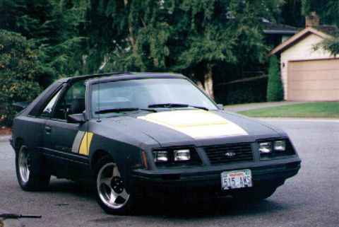 1983 Ford Bronco - This dark coupe features a yellow hood stripe and racing stripes on the fender, captured from a 3q-front perspective.
