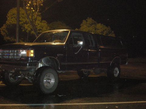 1991 Ford Bronco - This black extended cab pickup truck features a lifted suspension and is viewed from the front three-quarter angle at night.