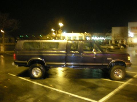 1991 Ford Bronco - A dark blue pickup truck with a camper shell is parked in a lot at night.