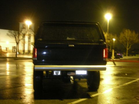 1991 Ford Bronco - A black SUV with a cap is seen from the rear at night in a wet parking lot.