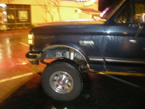 1991 Ford Bronco - A dark blue Ford F-350 truck is parked outside a building at night, with wet pavement reflecting lights.
