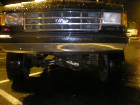 1991 Ford Bronco - Front view of a black 1991 Ford Bronco with a chrome grille and bumper, parked on a wet surface at night.