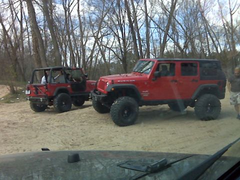 2008 Jeep Wrangler - Two red Jeep Wranglers are parked on a sandy trail surrounded by trees.