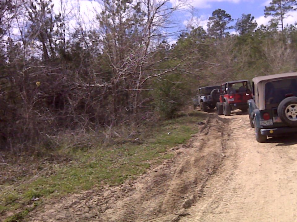 Several Jeeps driving on a muddy dirt road through trees