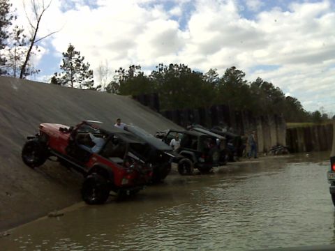 2008 Jeep Wrangler - Several Jeeps are parked in shallow water next to a concrete barrier, with one Jeep ascending a muddy slope.