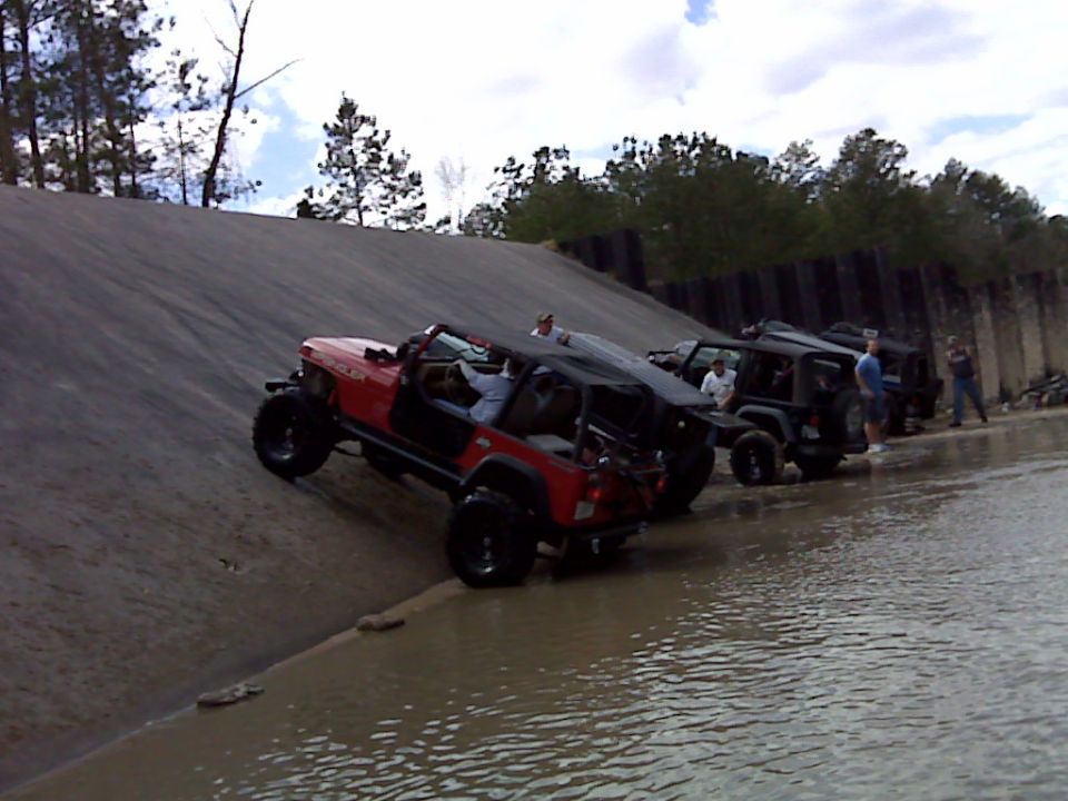 Red 2008 Jeep Wrangler climbing a muddy slope with other Jeeps behind
