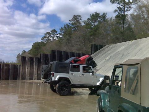 2008 Jeep Wrangler - Multiple Jeep Wranglers navigate a muddy, sandy terrain with a wooden barrier and a large incline.
