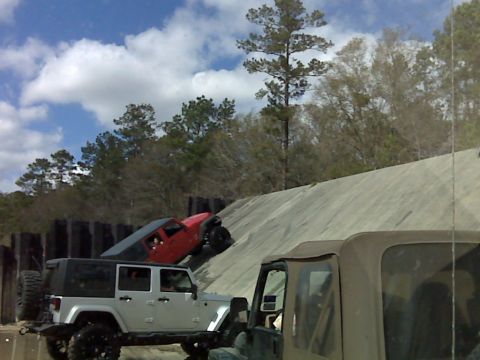 2008 Jeep Wrangler - A red two-door Jeep Wrangler climbs a steep concrete ramp at an off-road obstacle course while a lifted silver four-door Wrangler Unlimited…