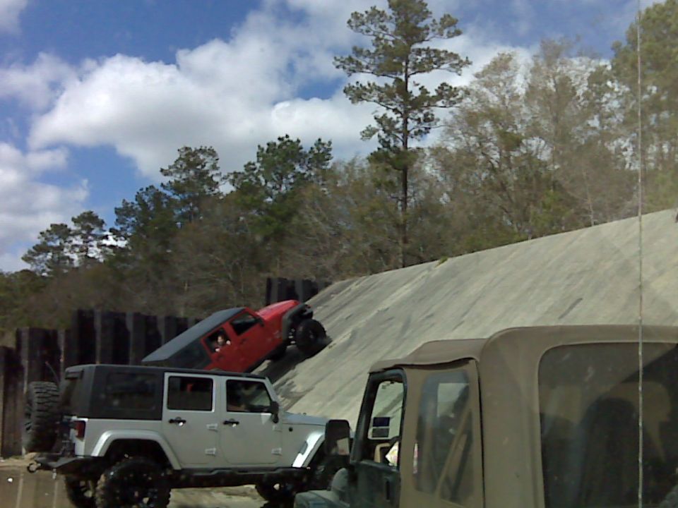 Red Jeep Wrangler climbing a concrete ramp with a lifted silver Wrangler Unlimited below