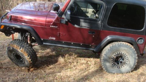 1995 Ford Bronco - A maroon Jeep Wrangler is shown with its front tire stuck in the dirt, highlighting its off-road capabilities.