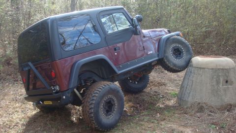 1995 Ford Bronco - A maroon Jeep Wrangler TJ navigates an off-road obstacle, with its front tire resting on a concrete structure.