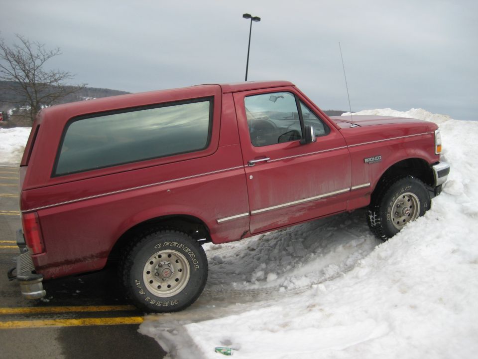 Red two-door Ford Bronco parked with front wheels on a snowbank, passenger side view