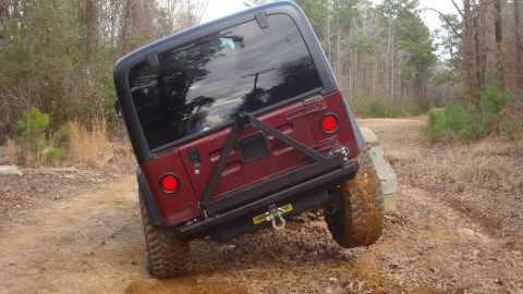 1995 Ford Bronco - A red Jeep Wrangler navigates a challenging dirt trail, its rear end tilted as it climbs over an obstacle.