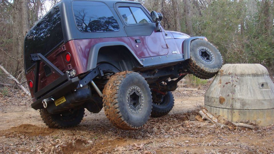 Maroon Jeep Wrangler TJ with lifted suspension climbing over concrete obstacle