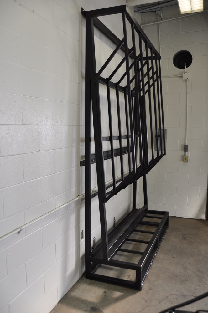 Black metal rack with vertical supports and horizontal shelves, leaning against a white brick wall