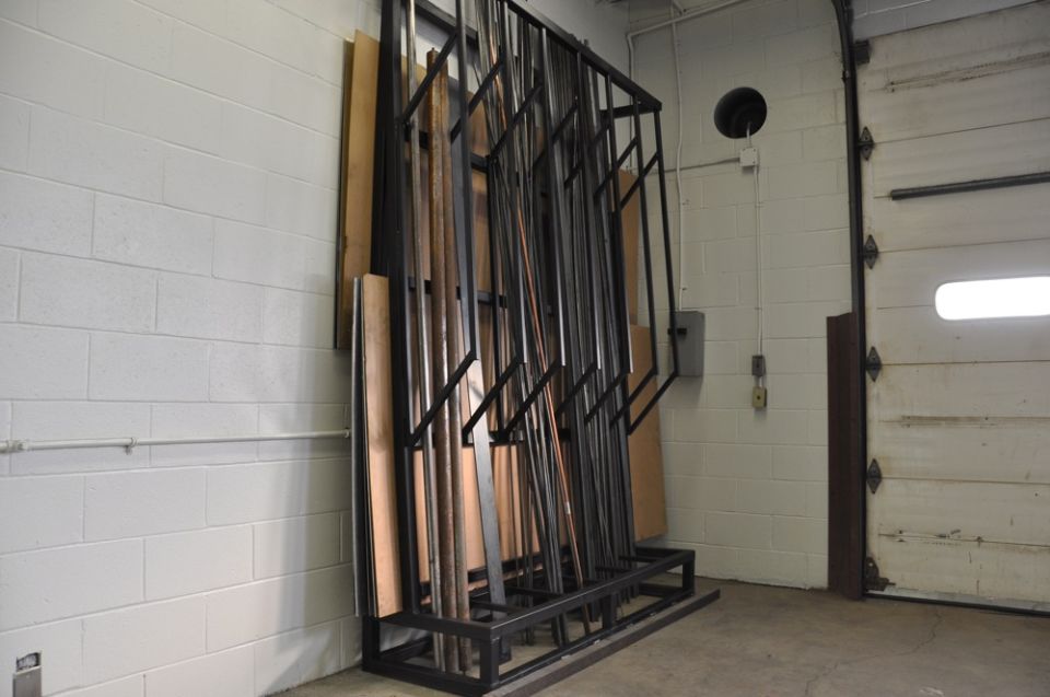 Rack holding metal and wood pieces against a cinder block wall next to a garage door