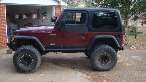 1995 Ford Bronco - A maroon Jeep Wrangler is parked outside a garage with a speed limit sign visible.