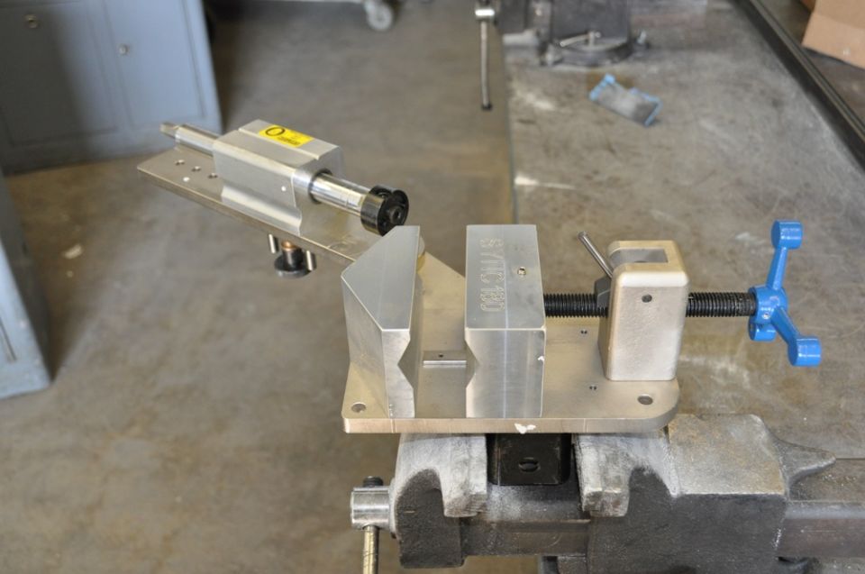 Metal vise holding a jig with a rotating spindle and a blue handle