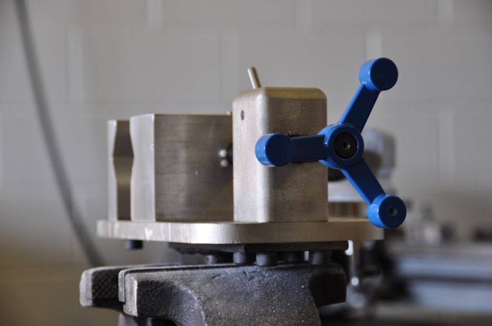 Metal vise with a blue three-spoke handle, mounted on a larger vise