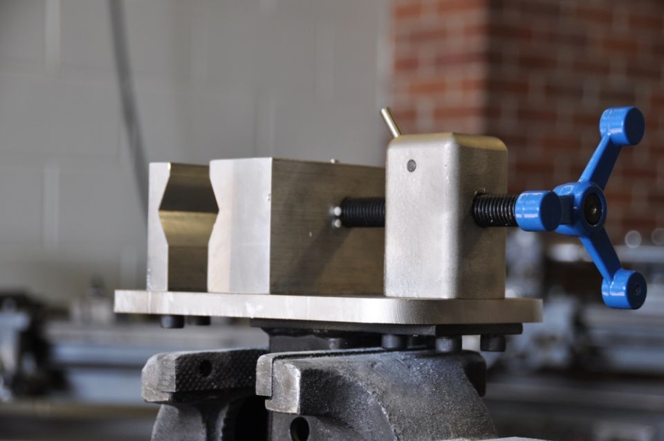 Close-up of a metal vise with a blue handle, clamped onto another vise