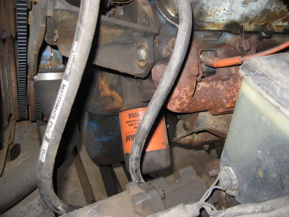 Close-up of a rusty engine bay with hoses and an oil filter.