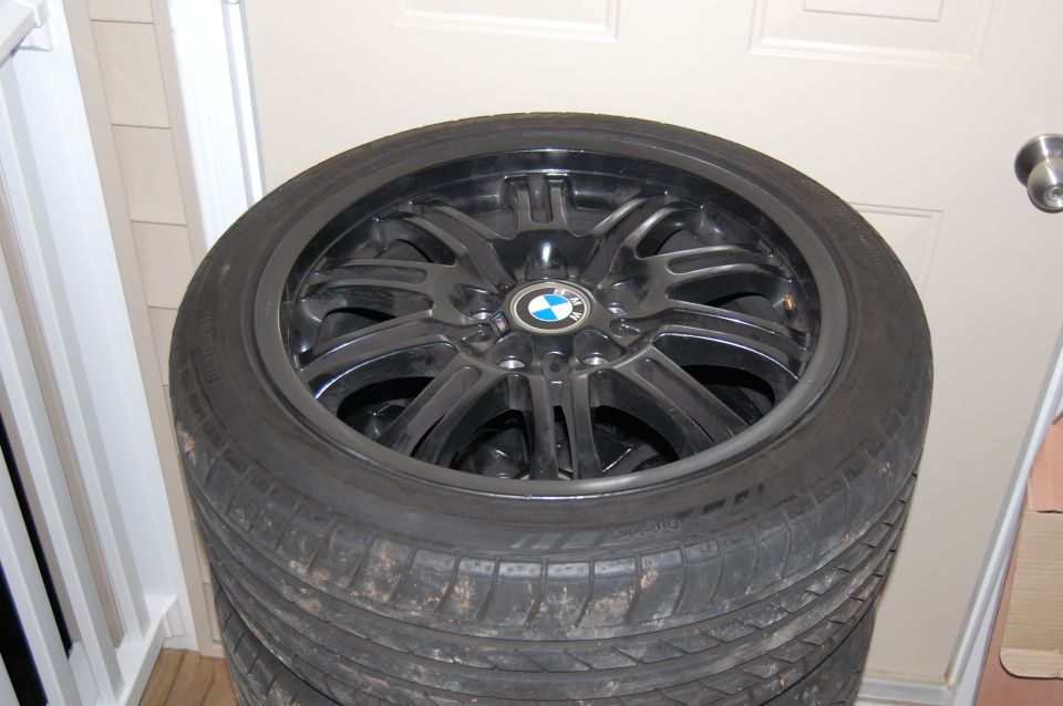 Stack of four black BMW M-style alloy wheels with Continental tires.
