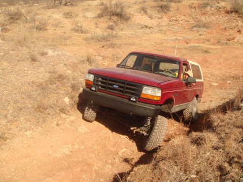 1992 Ford Bronco - A red 1992 Ford Bronco navigates a steep, dry, dirt path with its front-left tire elevated.
