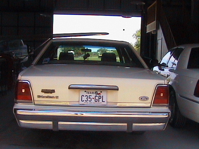 Rear of a cream Ford sedan with Texas plate C35-GPL parked in a shop