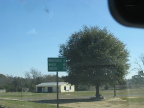 1988 Ford C-350 (Centurion Conversions) - A road sign indicates distances to nearby towns, with a large tree and a building in the background under a clear blue sky.