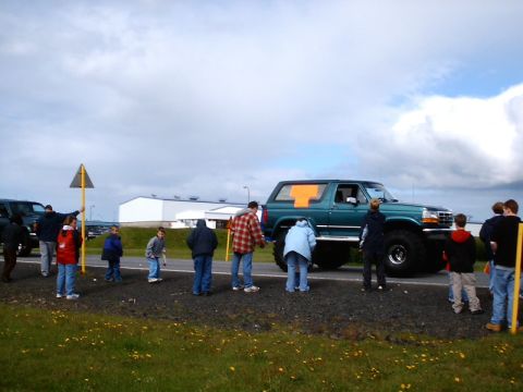 1996 Ford Bronco - A teal 1996 Ford Bronco with oversized tires and an orange 'T' graphic on the rear window is observed with a crowd gathered around.