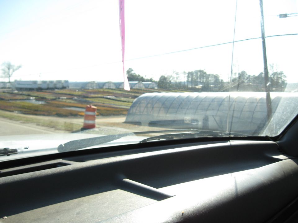 View from inside a vehicle looking out the windshield at greenhouses and fields