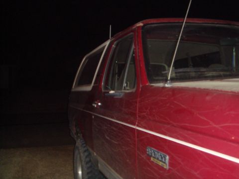 1992 Ford Bronco - A red Ford Bronco is shown from the side at night. The vehicle has a white stripe along the lower body and a "BRONCO" emblem visible on the…