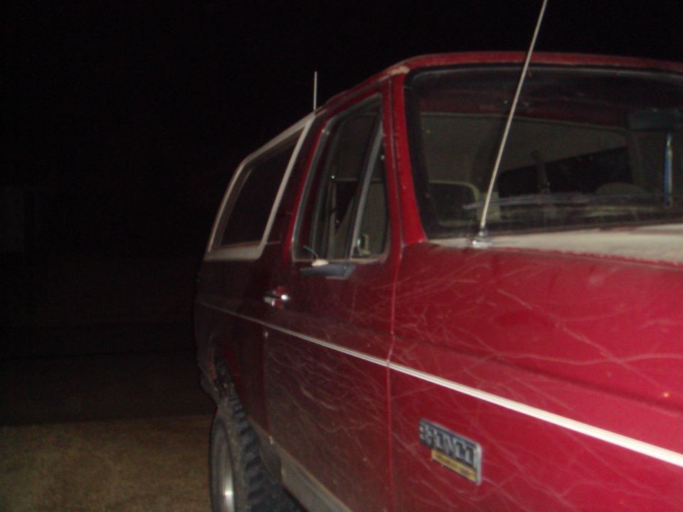 Red Ford Bronco side view at night with white stripe and Bronco emblem.