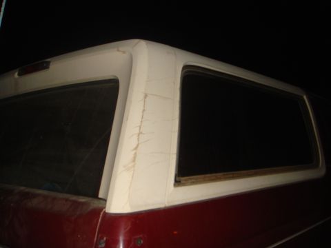 1992 Ford Bronco - The rear passenger side of a red and white SUV is shown at night. The white fiberglass top has visible scratches and dirt.