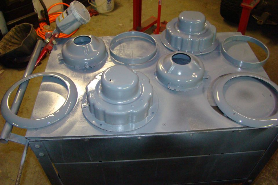 Gray painted metal parts laid out on a table with a spray gun in the background.