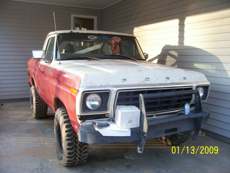 1980s Ford pickup truck, red and white, with off-road tires and black grille guard.