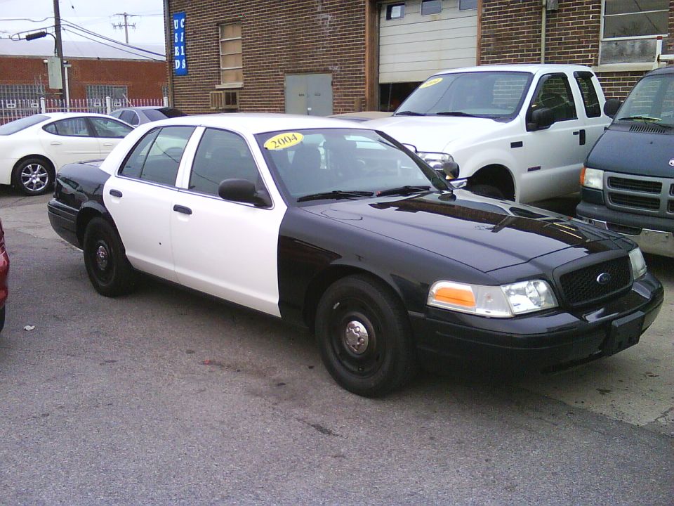Black and white Ford Crown Victoria sedan parked on asphalt.