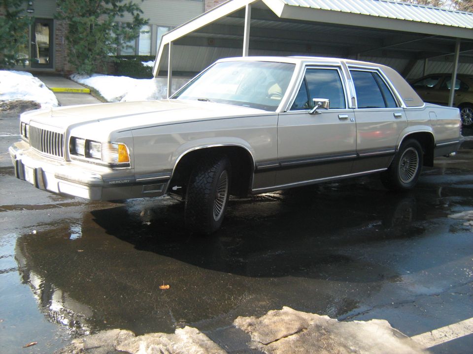 Front three-quarter view of a tan full-size sedan on wet pavement