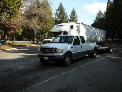 1991 Ford Bronco - A white Ford F-series pickup truck with a gray lower body trim tows a large white trailer. The truck is parked in a paved lot with trees an…