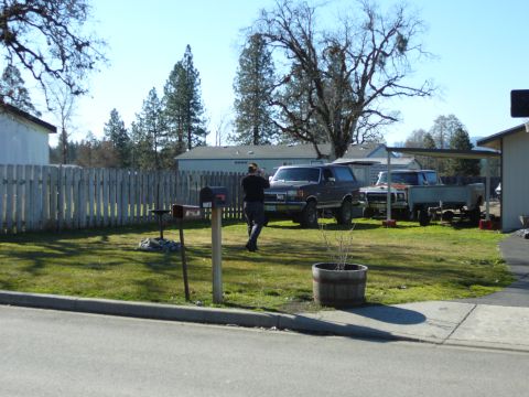 1991 Ford Bronco - A person stands in a grassy yard next to a dark gray Ford Bronco. Several other trucks and a utility trailer are parked in the background u…