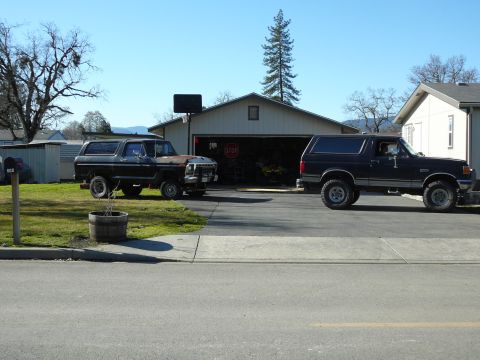 1991 Ford Bronco - Two Ford Broncos are parked in a driveway in front of a garage. The Bronco on the left is dark gray and black, while the Bronco on the righ…