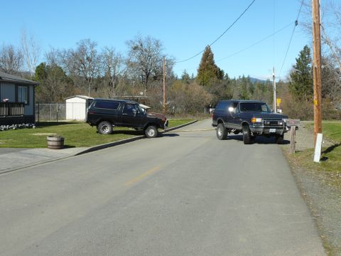 1991 Ford Bronco - Two Ford Bronco SUVs are parked on a paved road. The black Bronco is on the left, and a dark blue Bronco is on the right.