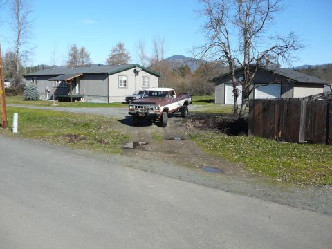 1991 Ford Bronco - A brown and white Ford pickup truck is parked on a gravel driveway in front of a gray house and a detached garage. The truck is viewed from…