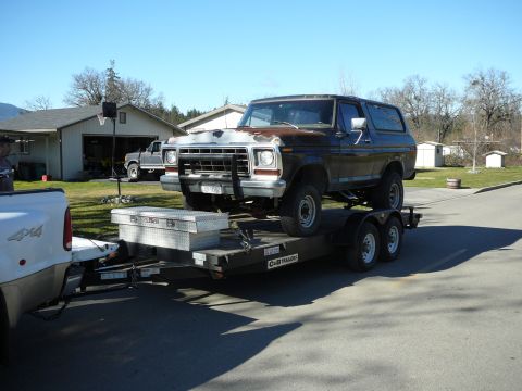 1991 Ford Bronco - A dark brown Ford Bronco is loaded onto a black dual-axle trailer, which is hitched to a white pickup truck. A silver toolbox is secured to…