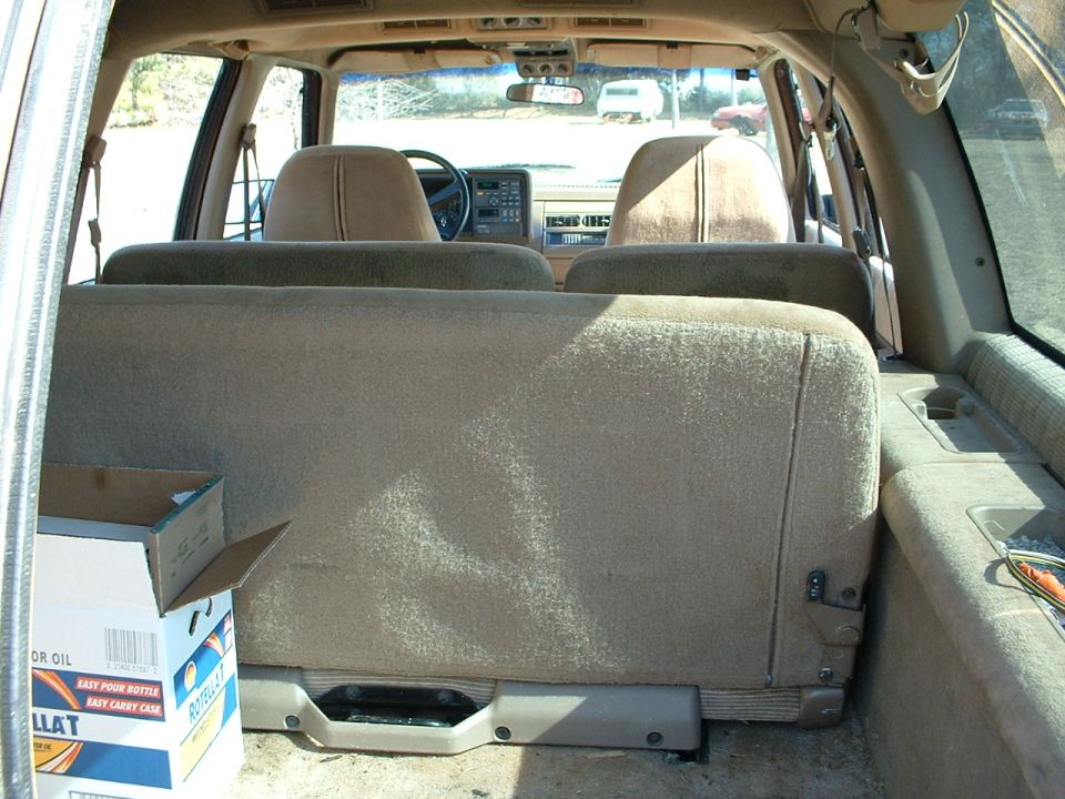 Cargo-area view of tan SUV interior with rear bench seat and case of motor oil