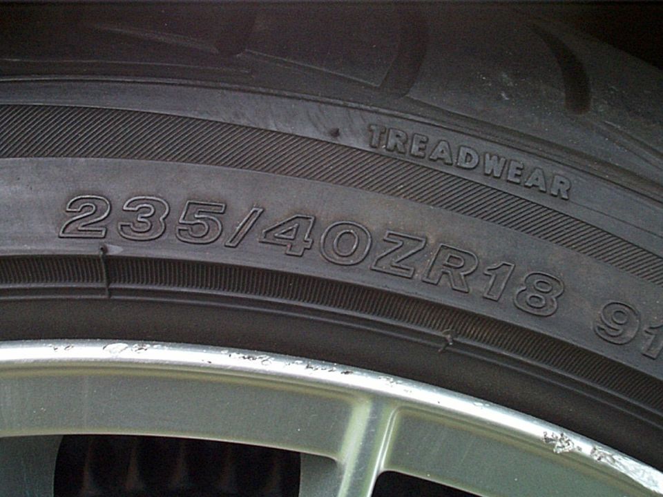 Tire sidewall stamped 235/40ZR18 on a silver alloy wheel with curb rash on the rim lip