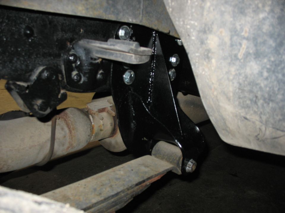Vehicle frame with black bracket, leaf spring, exhaust pipe, and tire.